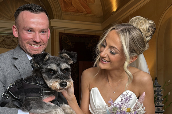 Bride and groom smile while groom holds dog